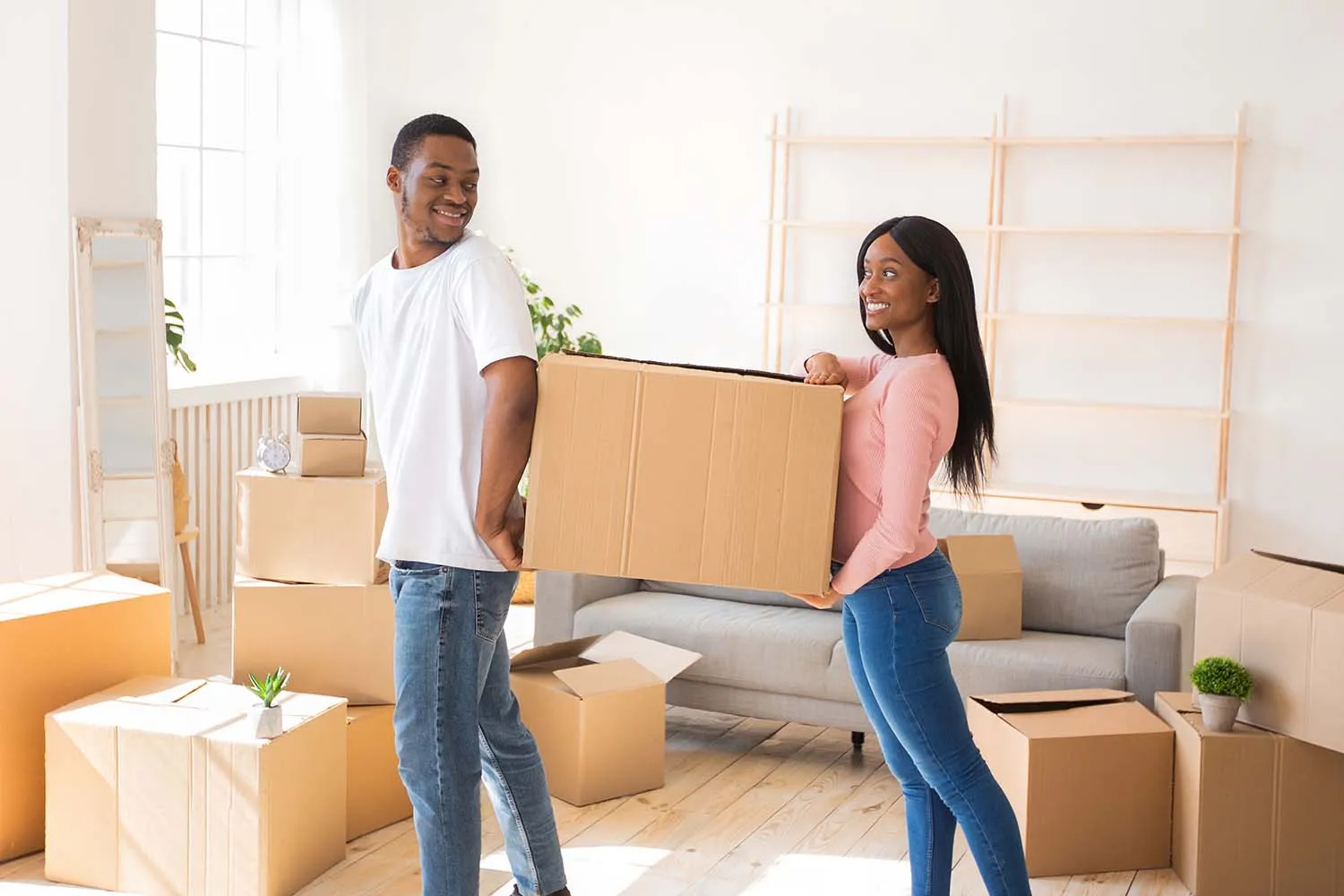 Loving black couple carrying cardboard box together, helping each other in their new home on moving day